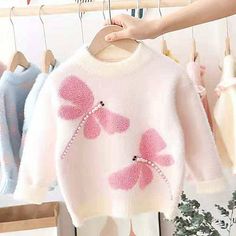 a sweater with pink bows on it hanging from a rack in front of other clothes