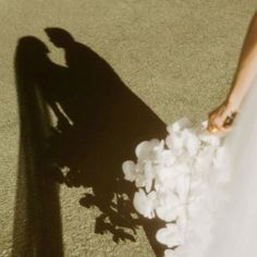 the shadow of a person in a wedding dress holding a bouquet of white flowers and petals