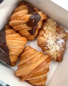 four pastries in a box with chocolate and almond toppings on the top one