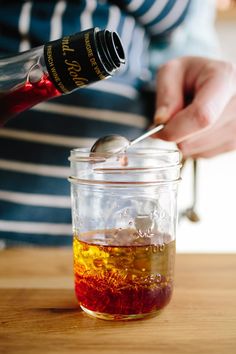 a person pouring liquid into a glass jar on top of a wooden table with a spoon