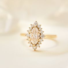 a yellow gold ring with an oval shaped diamond surrounded by smaller round diamonds on a white background