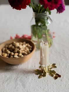 flowers and candles on a table next to a bowl with nuts in it, including red carnations