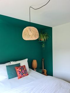 a bedroom with green walls, white bedding and a guitar hanging from the ceiling