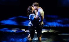 a man and woman kissing on stage with blue lights in the backround behind them