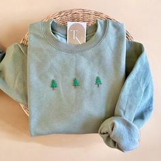 a green sweater with trees embroidered on the front and back, sitting next to a wicker basket