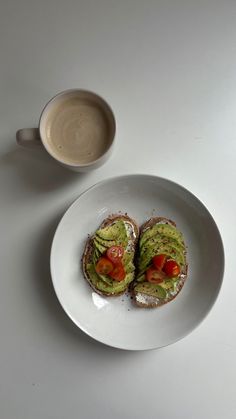 an avocado and tomato sandwich on a white plate next to a cup of coffee