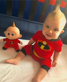 a baby sitting on top of a bed next to a stuffed toy doll wearing a red shirt