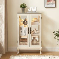 a white cabinet with glass doors and shelves in the corner next to a potted plant