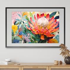 an art print on the wall above a wooden cabinet with a vase and potted plant