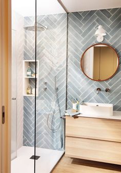 a bathroom with blue and white tiles on the wall, wooden cabinets and a round mirror