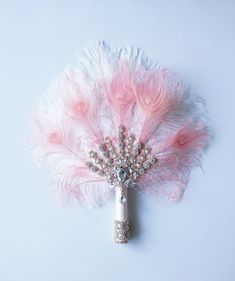 a pink and white feather brooch with some beads on the end, sitting on a light blue surface