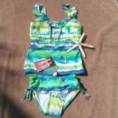 This Cute Tankini Set Features A Top That Has Ruffles At The Neck. Faux Tie In Front. Ties At Neck. Bottoms Have Rouched Sides. Both Top And Bottom Feature Silver Peace Sign Accents. Fully Lined. Playful Blue Tankini For Swimming, Blue Playful Tankini For Beach Season, Playful Blue Tankini For Beach Season, Playful Green Tankini For Poolside, Blue Summer Tankini For Playwear, Playful Green Tankini For Swimming, Blue Stretch Tankini For Playwear, Playful Blue Fitted Tankini, Spring Blue Tankini For Playwear