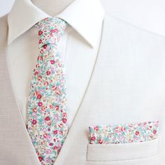 a man wearing a white suit and floral tie with matching pocket square in his lapel