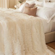 a bed with white blankets and pillows on top of it next to a vase filled with flowers