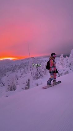 a person riding a snowboard on top of a snow covered slope in the evening