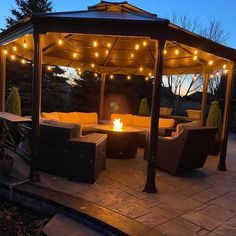 an outdoor gazebo with string lights on the roof and patio furniture around it at night