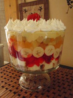 a cake with white frosting and fruit toppings in a glass dish on top of a wooden table