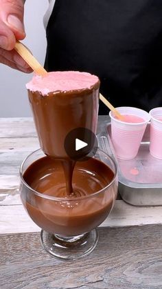 a person pouring chocolate into a bowl with pink cups in the background on a wooden table