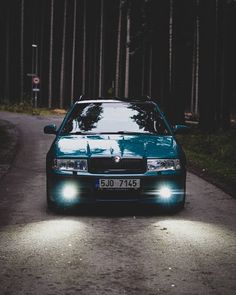 a blue car parked on the side of a road at night with its lights on