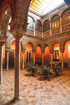 the inside of an old building with columns and arches on it's sides, surrounded by potted plants