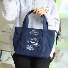 a person holding a blue bag with snoopy on it's side and wearing black pants