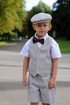 a young boy wearing a gray suit and bow tie standing in the middle of a street