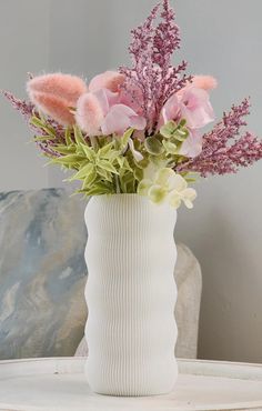 a white vase filled with pink flowers on top of a table