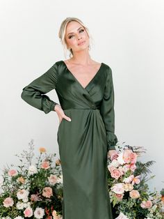 a woman standing in front of flowers wearing a green dress with long sleeves and an asymmetrical neckline