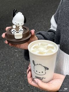 a person holding a cup with some kind of drink in it's hand and a toy cow on the lid