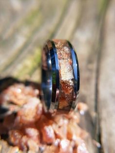 a wedding band with blue and black ceramic inlays sits on top of some rocks