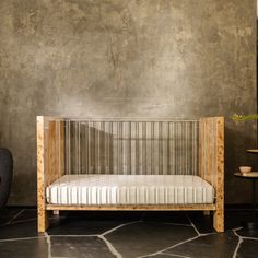 a small wooden crib sitting on top of a stone floor next to a chair