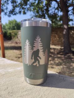 a yeti cup sitting on top of a stone wall with trees in the background