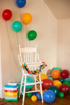 a white chair sitting in front of a bunch of colorful balloons on top of a hard wood floor