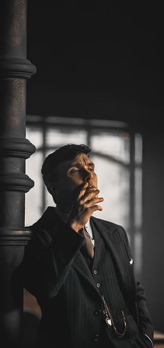 a man in a suit is talking on his cell phone while leaning against a pole