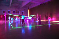 some people are dancing in a large room with neon lights on the floor and one person is holding a frisbee