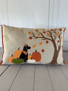 a decorative pillow with a dog and pumpkins on the front, sitting on a wooden floor