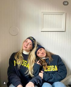 two young women sitting on the floor in front of a door wearing sweatshirts and beanies