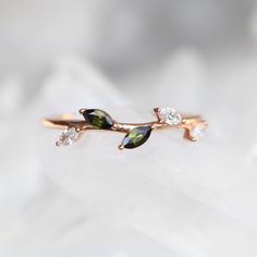 a rose gold ring with two green leaves and three white diamonds on it's side