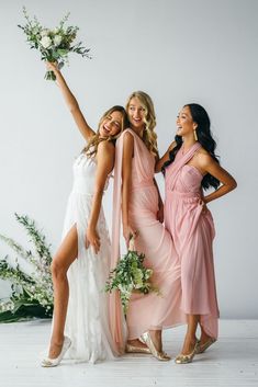 three bridesmaids pose with their bouquets in front of the camera and one is holding her hand up