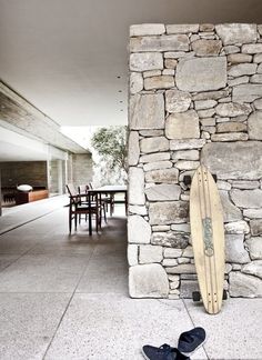 a surfboard leaning against a stone wall in front of a dining room table and chairs