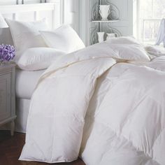 a bed with white comforters and pillows in a room next to a night stand