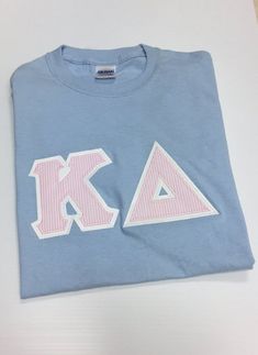 a blue t - shirt with the letters k and a pink letter on it