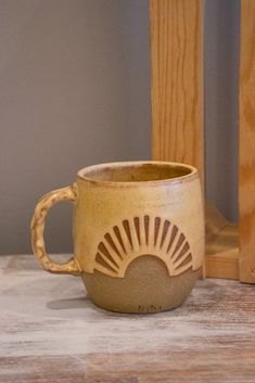 a coffee cup sitting on top of a table next to a wooden chair and shelf