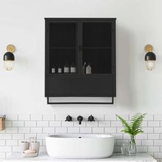 a white sink sitting under a black cabinet next to a green plant in a vase