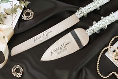 two knifes with name tags on them sitting next to some pearls and other jewelry