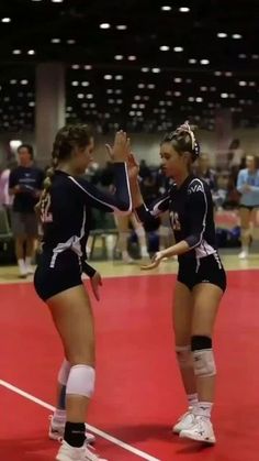 two female volleyball players standing on a court with their hands in each other's pockets