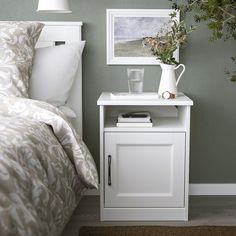 a white nightstand sitting next to a bed in a room with green walls and pillows