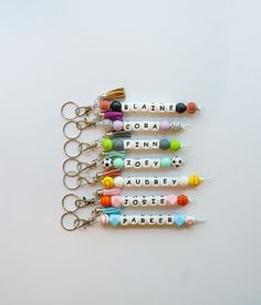 six different colored beads are hanging from keychains on a white surface with the words please, deare, flora, finnn, robert and albert written in small letters