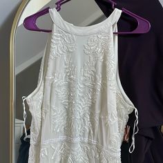 a white dress hanging on a hanger in front of a mirror with purple clothes