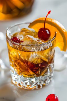 a glass filled with ice and cherries on top of a white table next to two orange slices